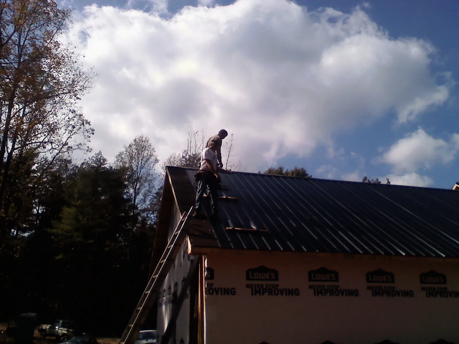Roofer fastening dark metal panels high against a cloudy sky, from a Roof Inspection job in Passaic