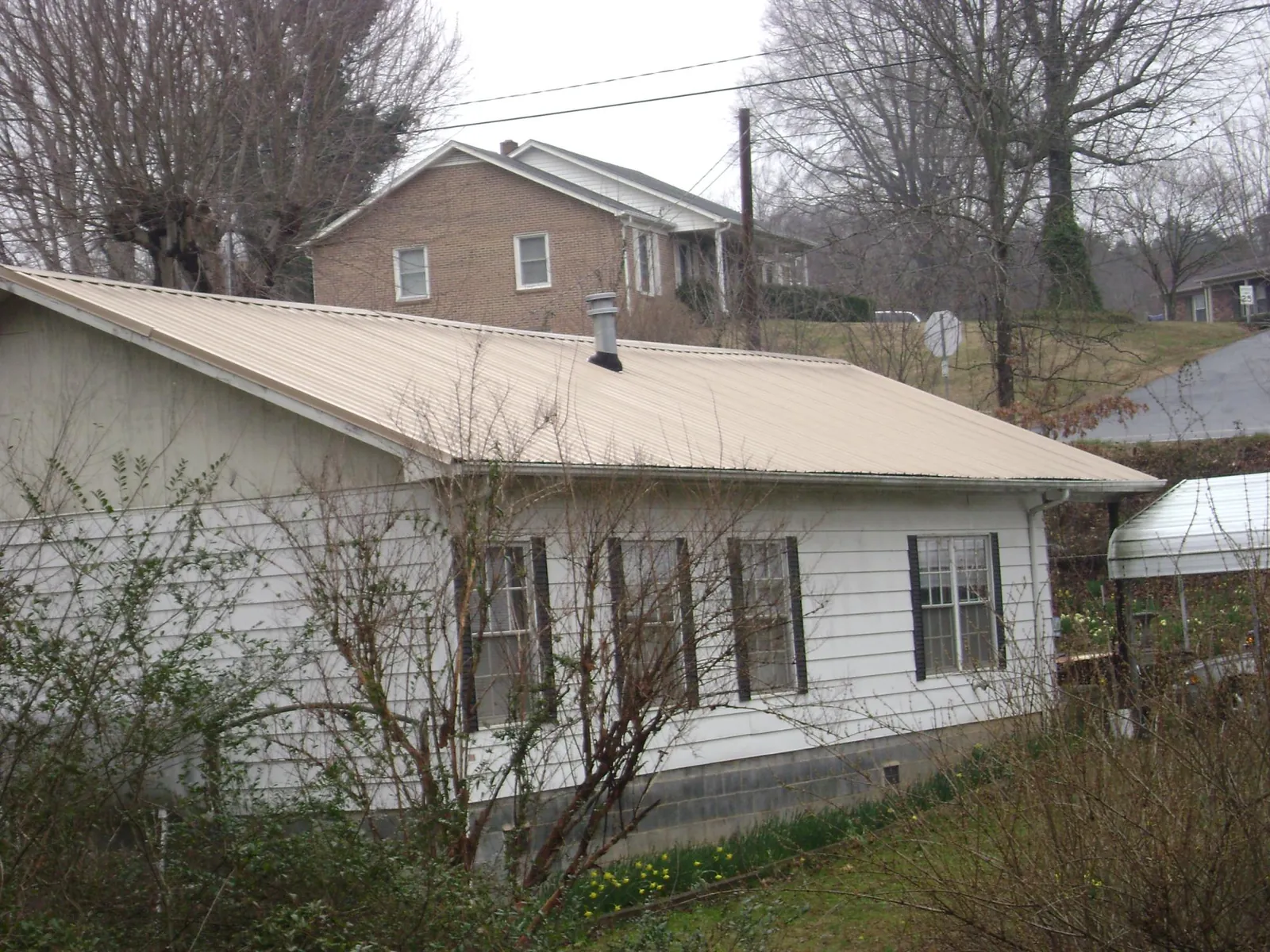 Tan metal roof on a white sided house set into a hillside — Commercial Roofing by Roofing Brothers in Passaic